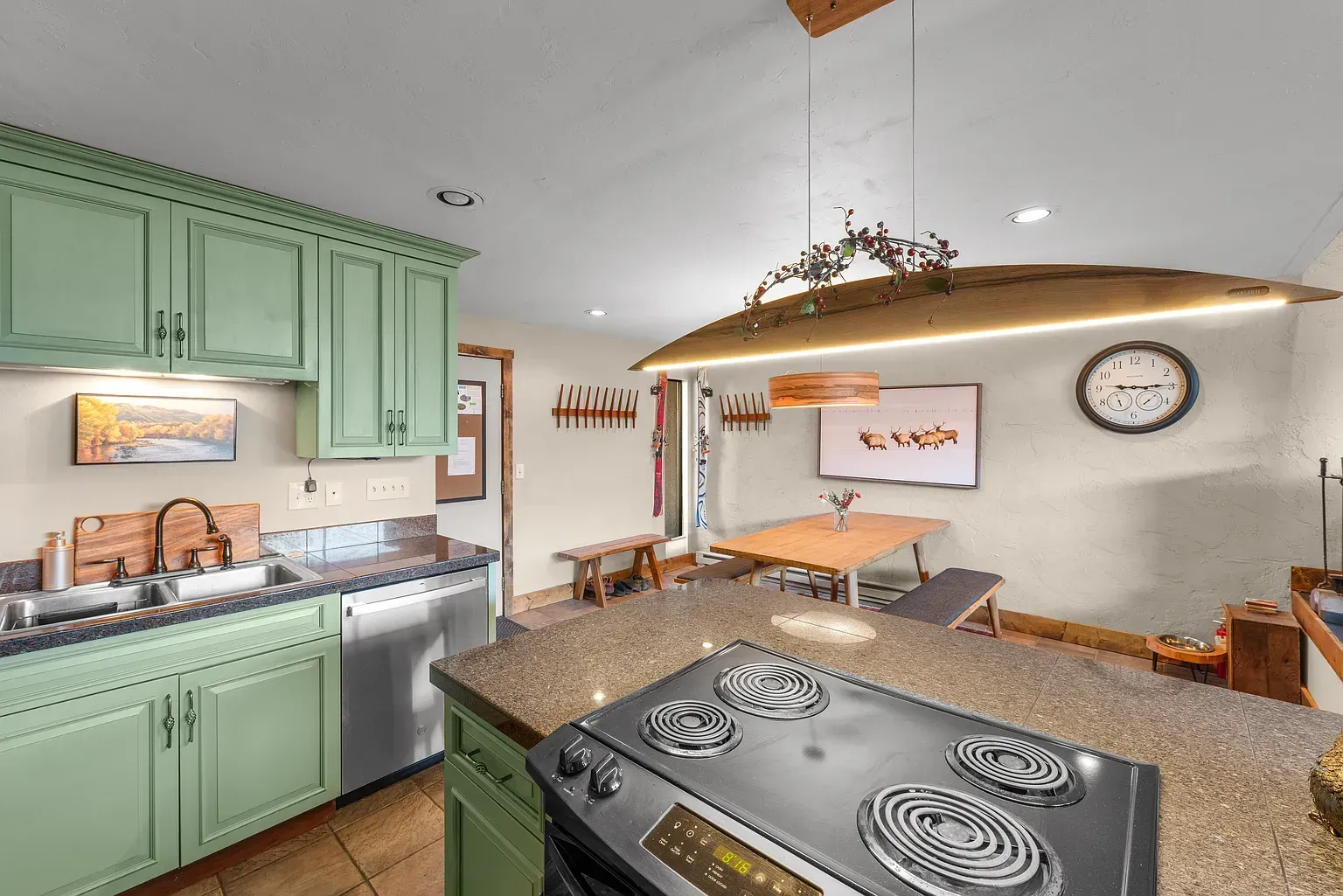 Bright kitchen with mint cabinets, granite island, stainless dishwasher, and dining nook under hanging lights