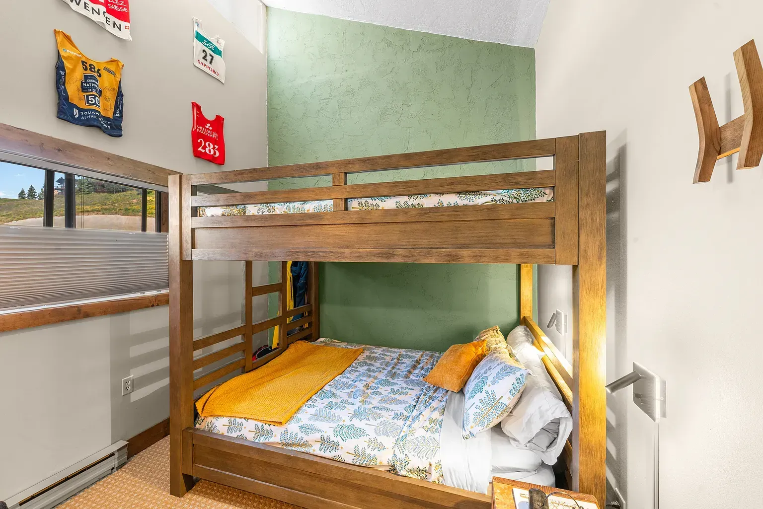 Small bunk bed in a bright room with green walls and orange bedding near a window