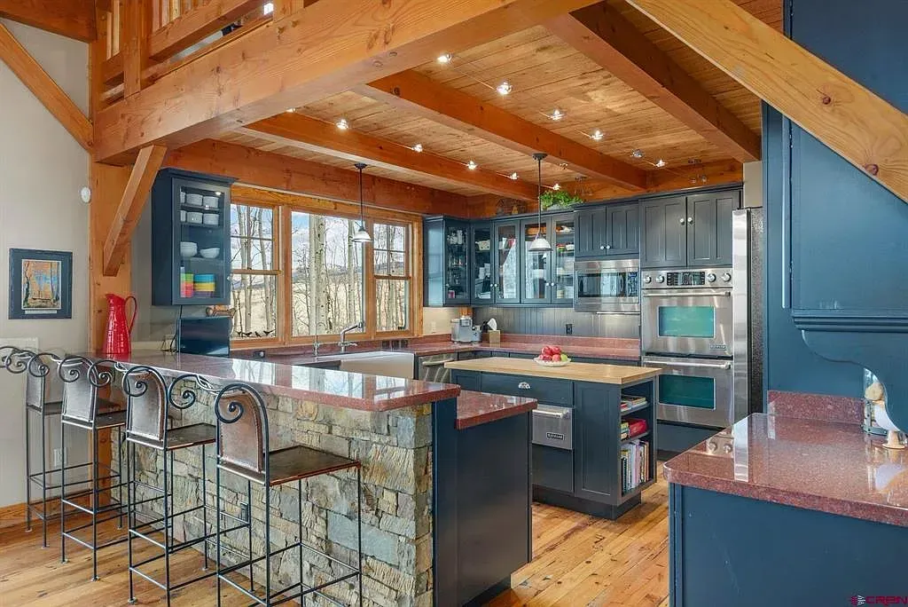 Modern kitchen with wood beams, blue cabinets, granite island, and barstools