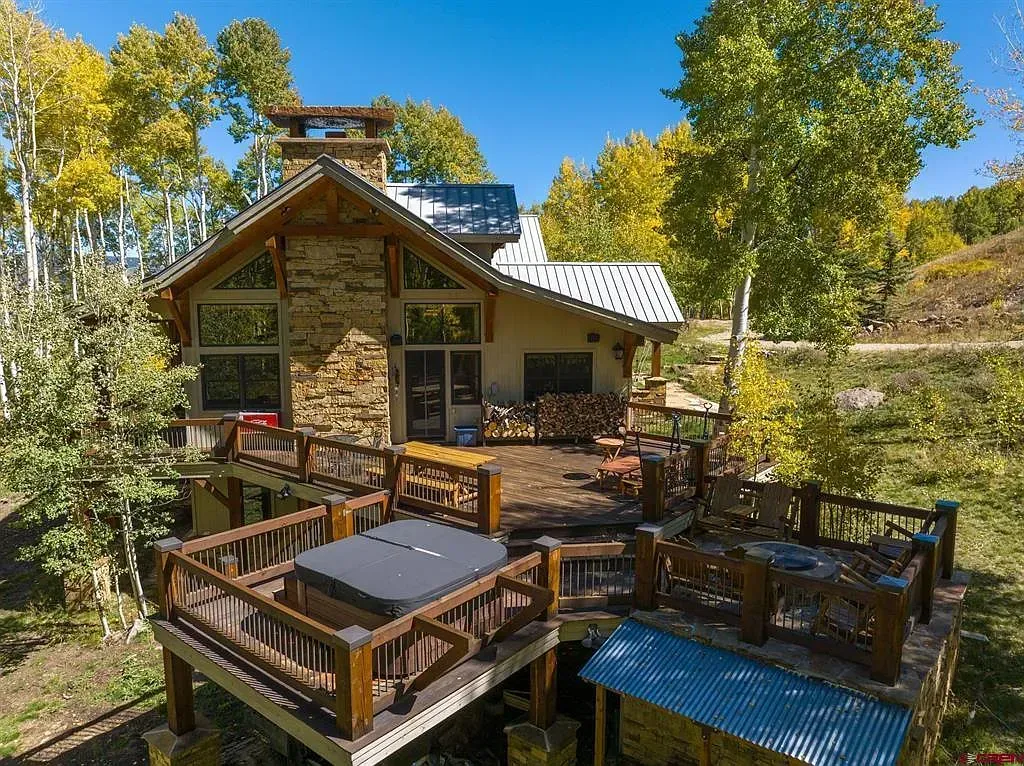 Rustic cabin deck with wooden table and chairs, surrounded by autumn trees under a bright blue sky