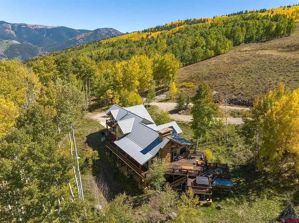 Aerial view of a rustic cabin in a yellow autumn forest with mountains in the background