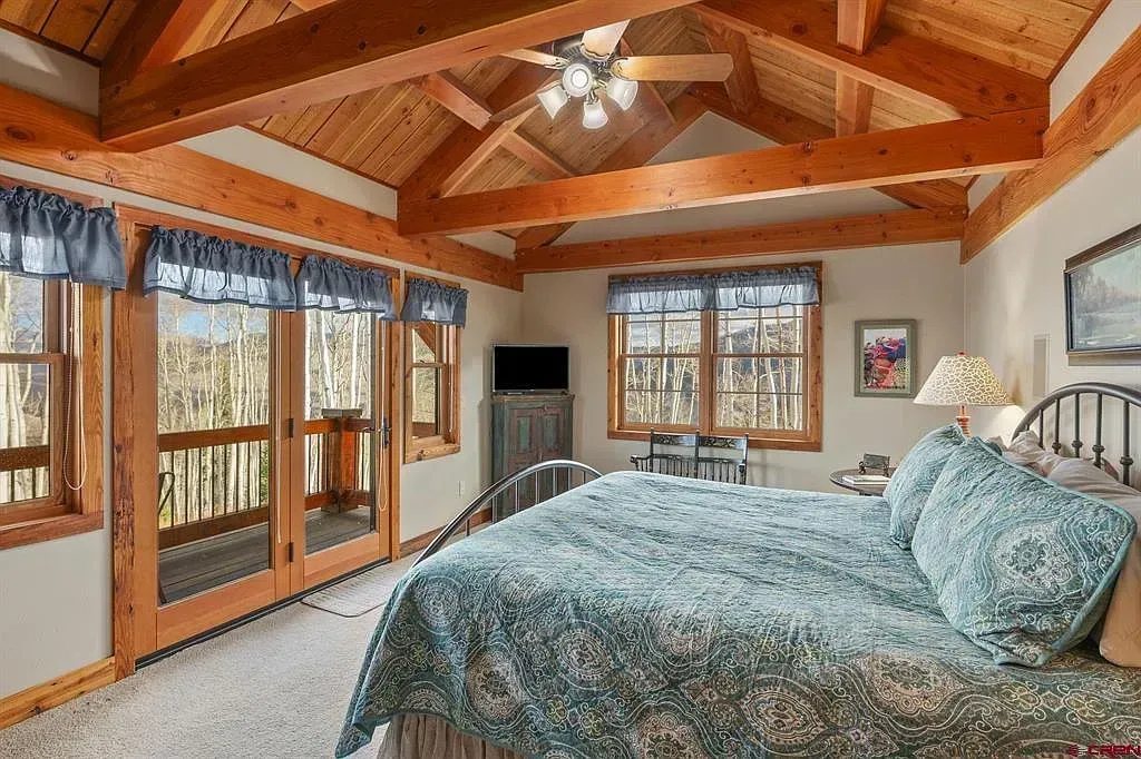 Cozy bedroom with vaulted wood ceiling, large windows, and a bed with blue bedding