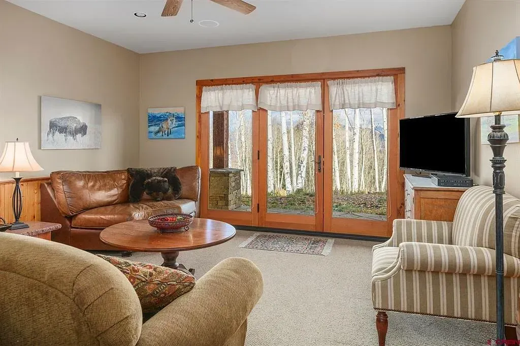 Cozy living room with sofa, armchair, coffee table, fireplace, and large windows with curtains.