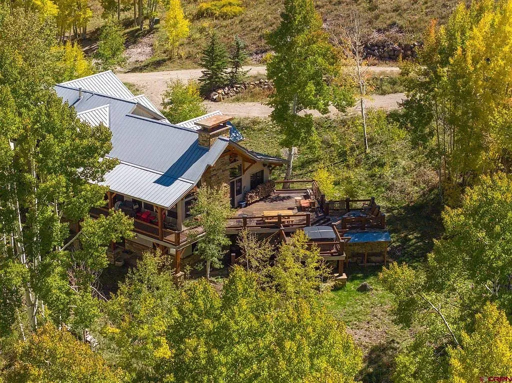 Rustic cabin with a metal roof nestled among dense green trees in a wooded hillside.