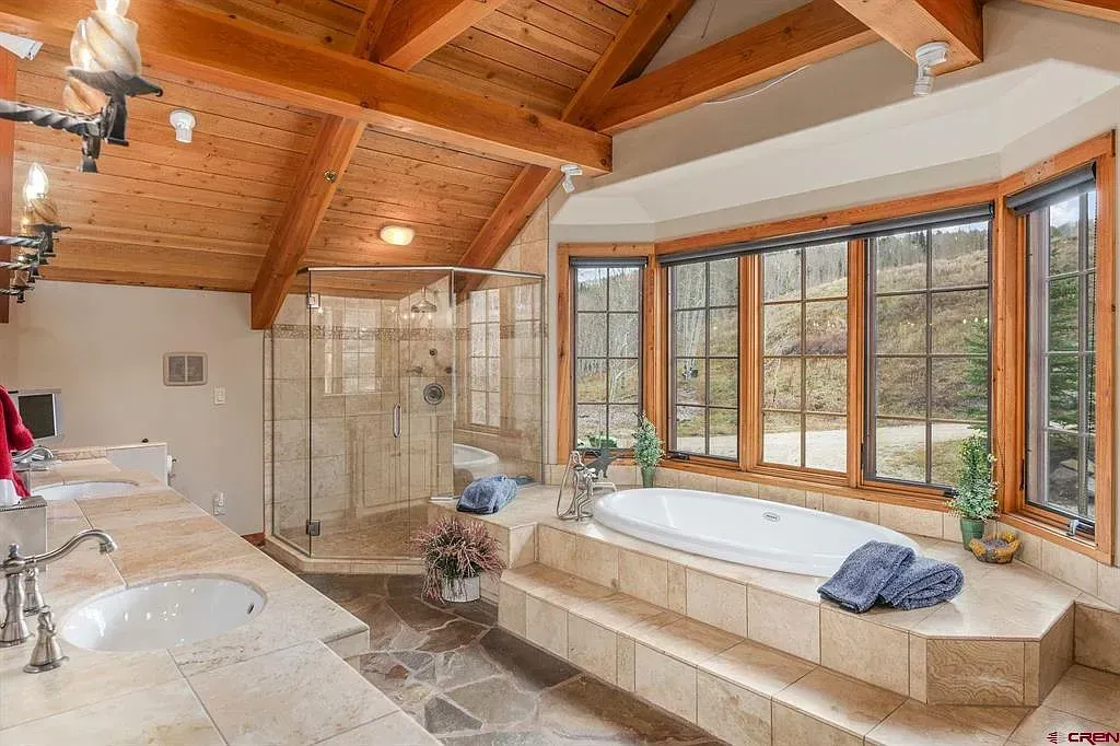 Bright bathroom with wooden ceiling, large windows, tiled soaking tub, and sink counter.
