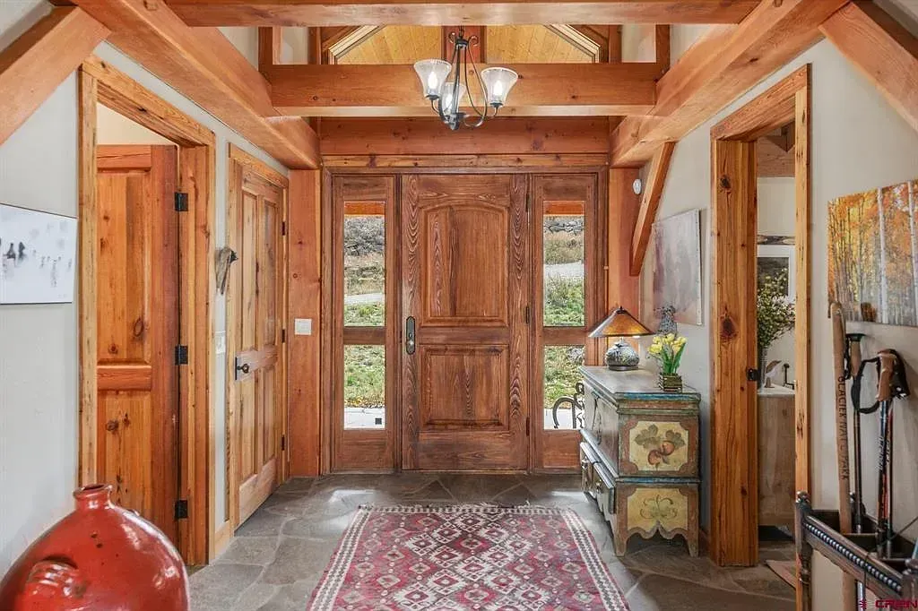 Wood-paneled entry hall with double front doors, red rug, and decorative console table.