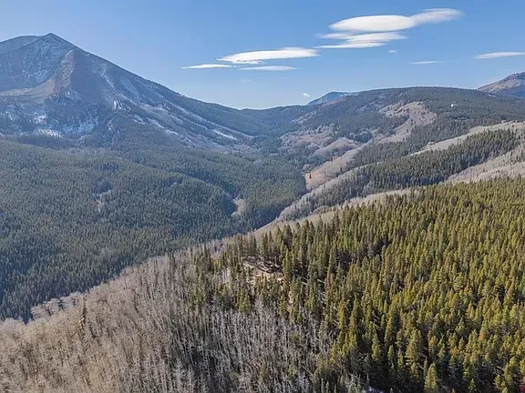 Mountain valley with forested slopes, a rocky peak, and cloudy blue sky