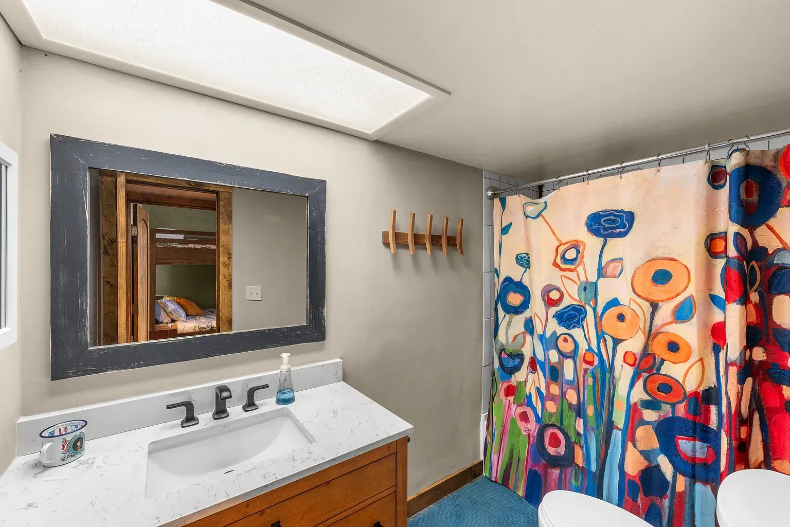 Bathroom with sink and mirror, colorful floral shower curtain, and bright overhead light.