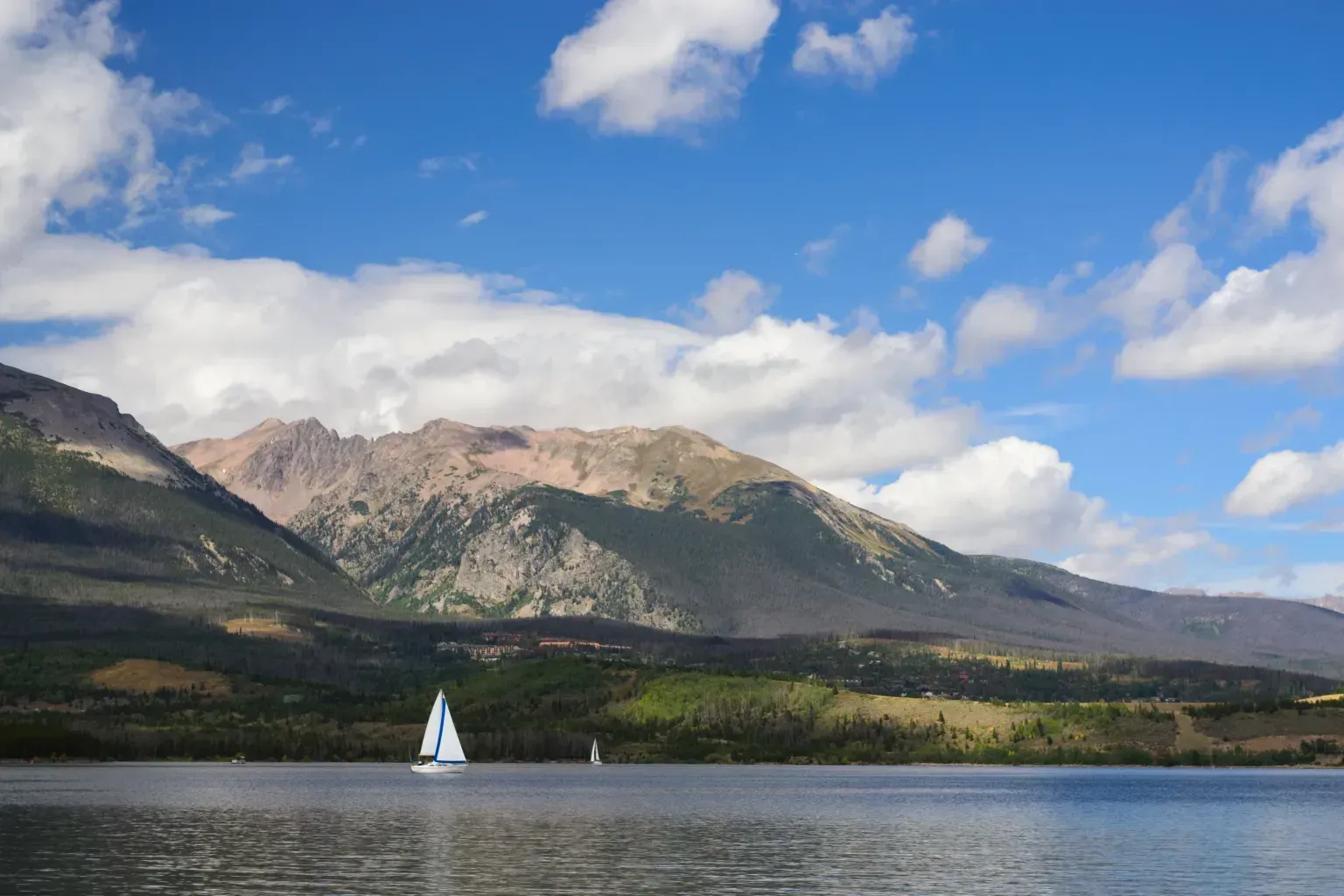 Sailboat on a calm lake with mountains and clouds under a blue sky