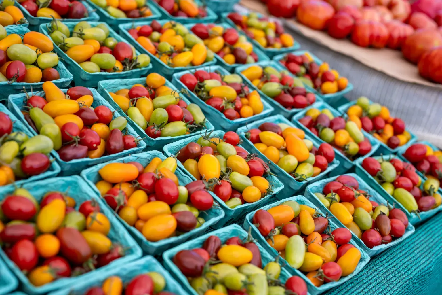 Crates of colorful mixed fruits arranged on a market table, including berries, apples, and peaches