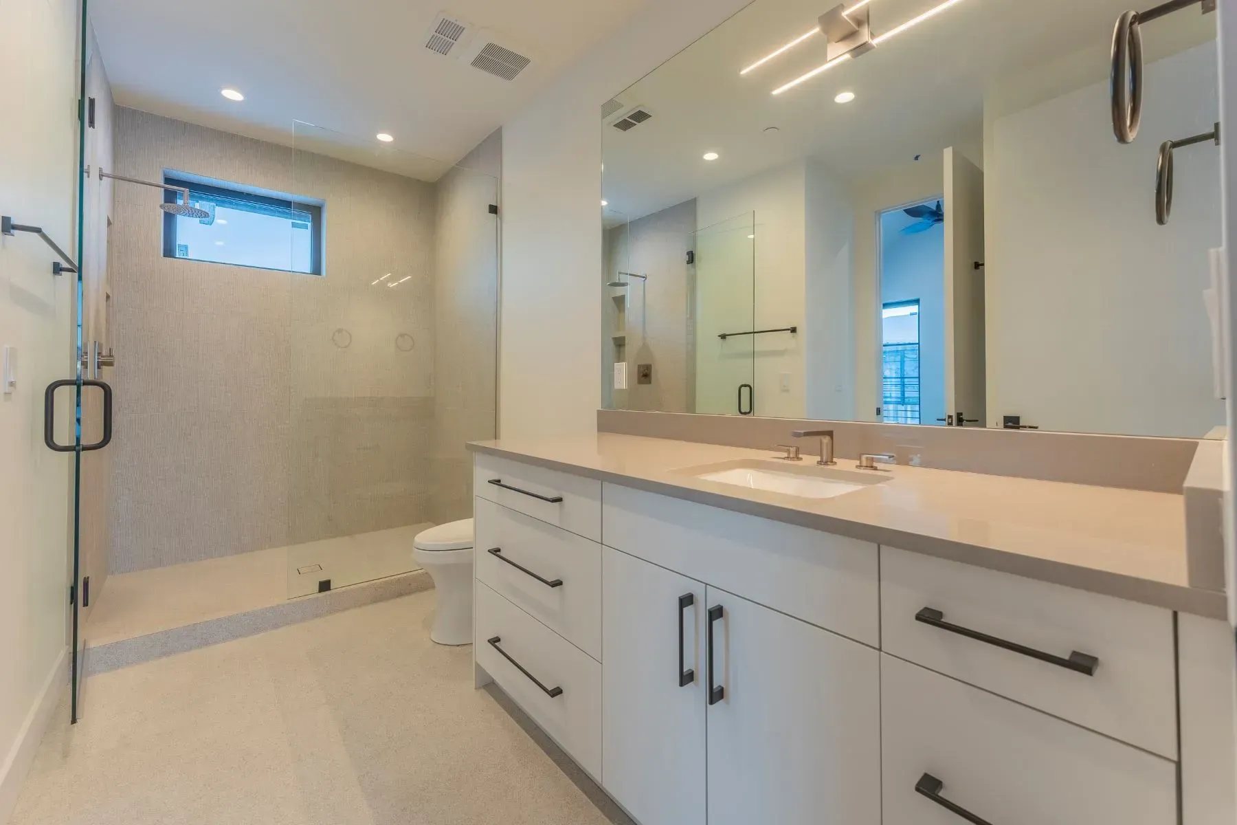 Modern bathroom with large vanity mirror, white cabinets, and a glass walk-in shower.