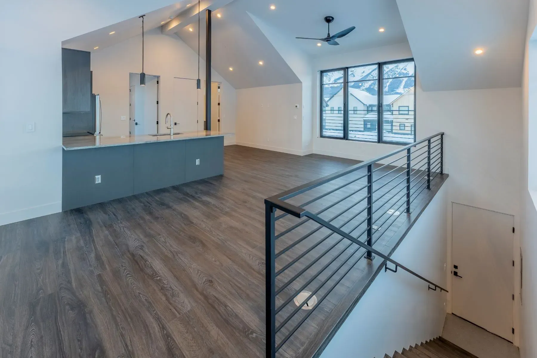 Modern open loft interior with gray floors, vaulted ceiling, and metal railing overlooking a stairwell