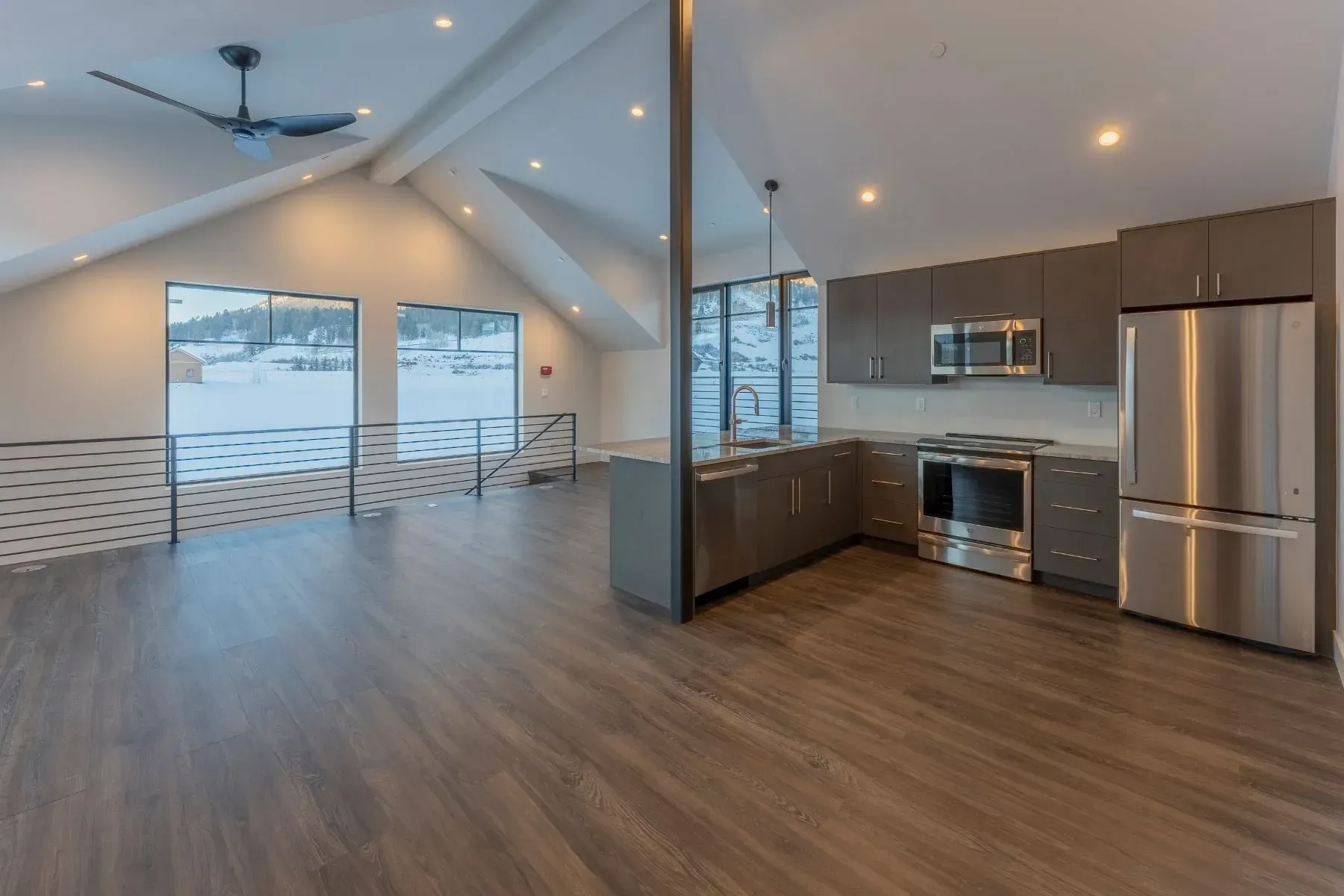 Open-concept living room and kitchen with wood floors, gray cabinets, stainless steel appliances, and large windows.