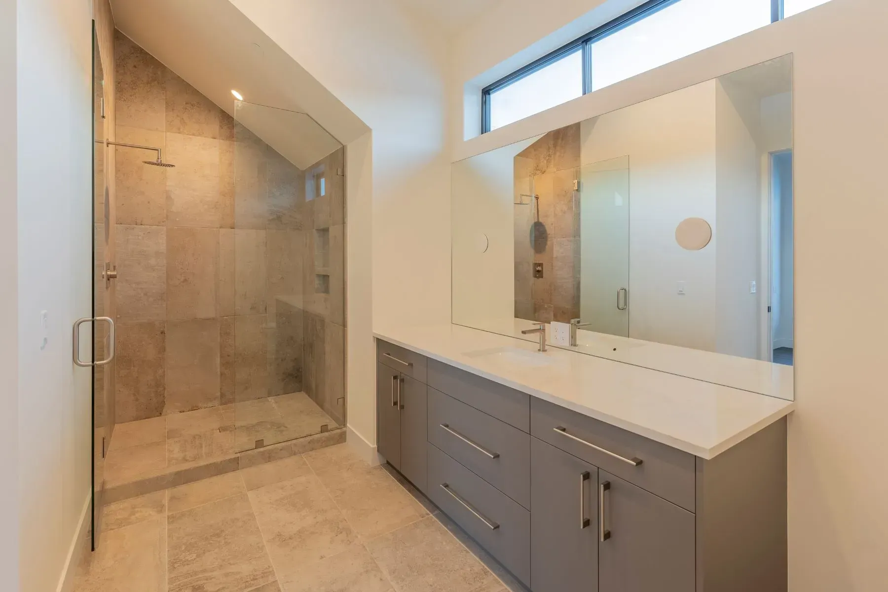 Modern bathroom with walk-in shower, double vanity, large mirror, and high window