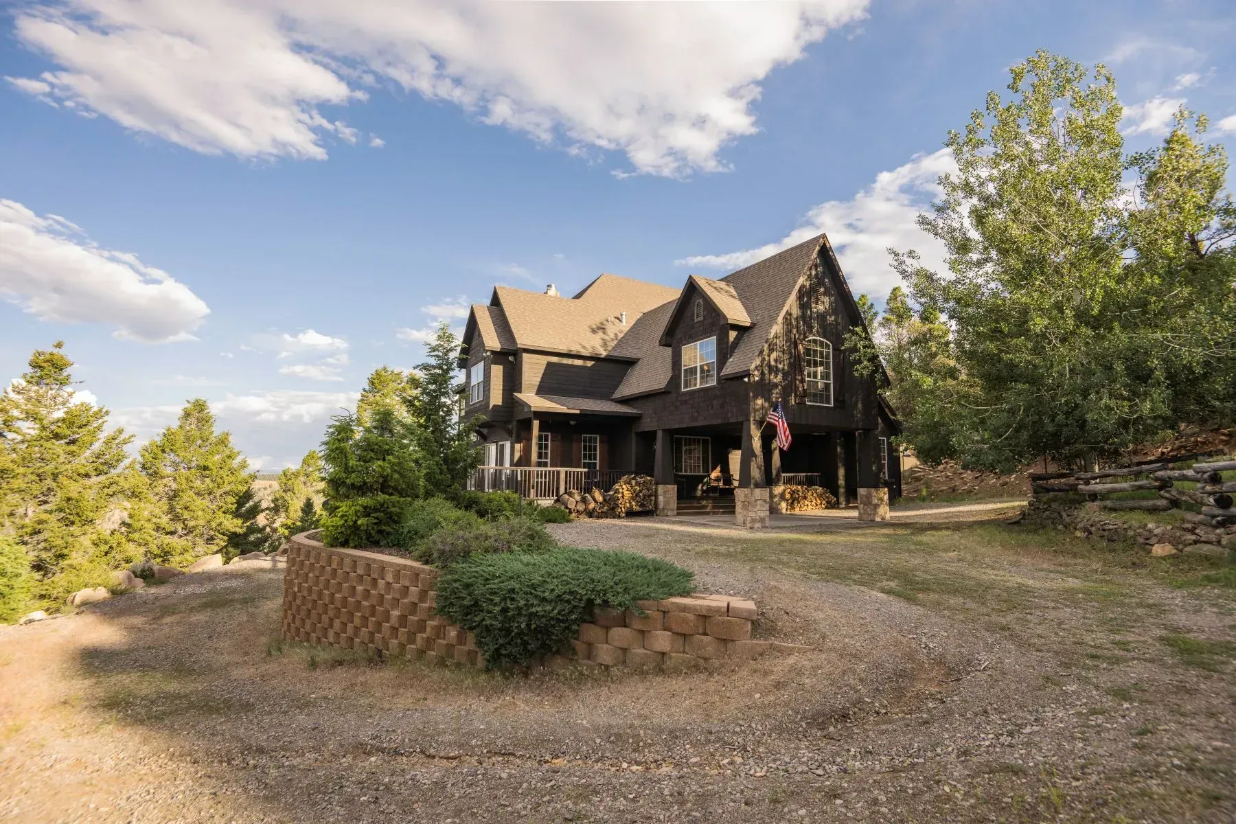 Large rustic house with stone and wood exterior, gravel driveway, and trees under a blue sky