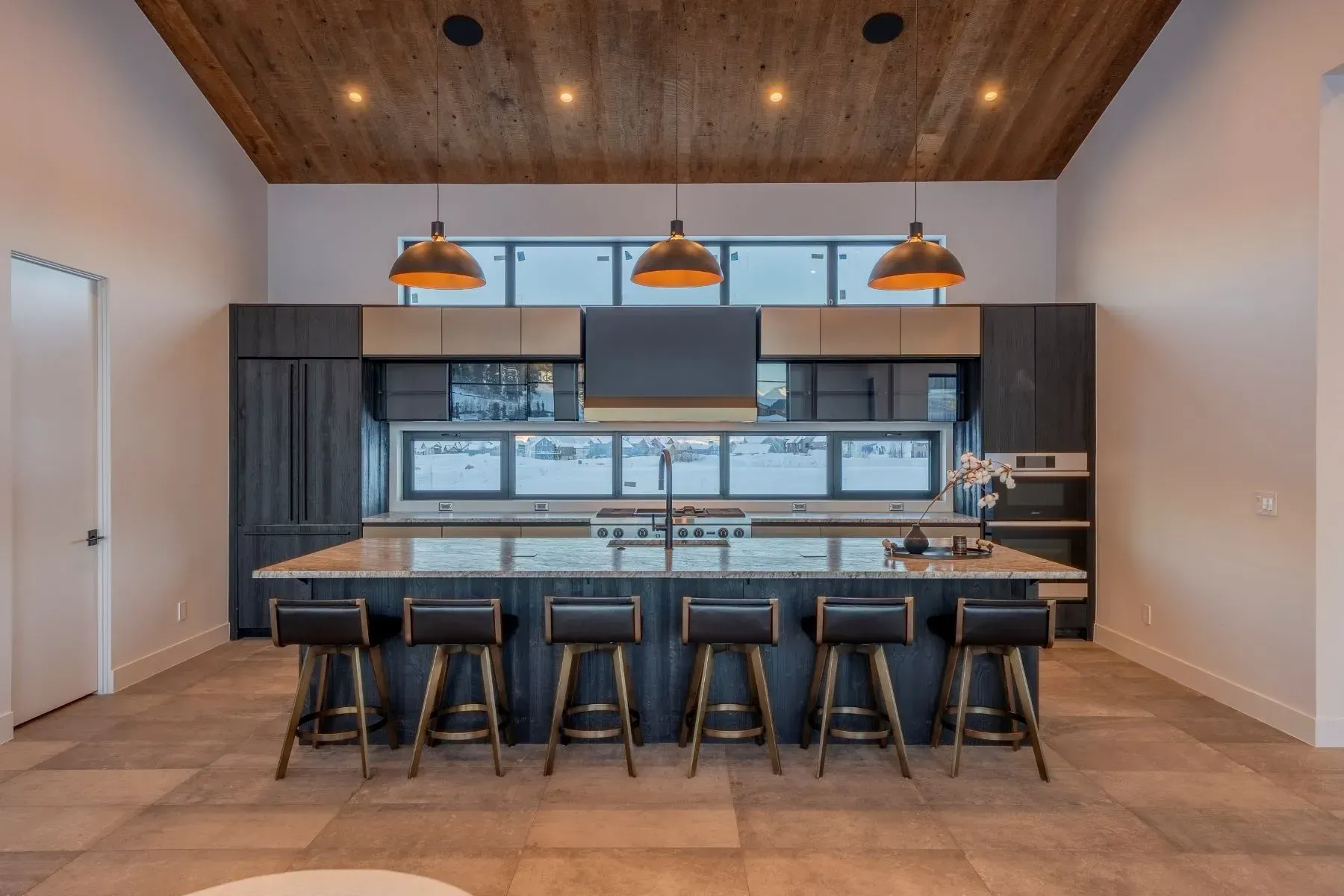 Modern kitchen with dark cabinets, island seating, pendant lights, and a wood-paneled ceiling