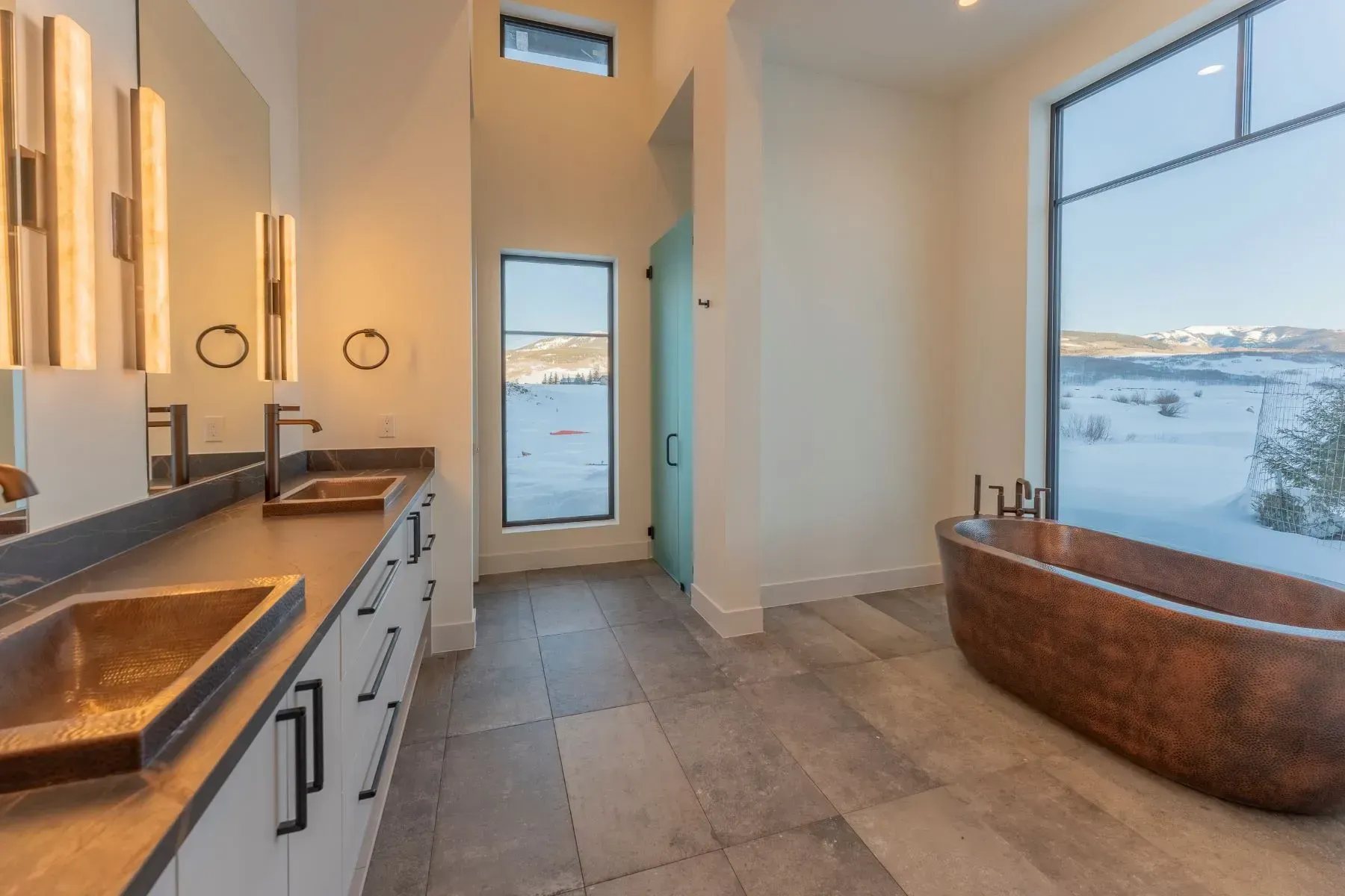 Modern bathroom with double vanity, large mirror, and soaking tub overlooking a snowy landscape