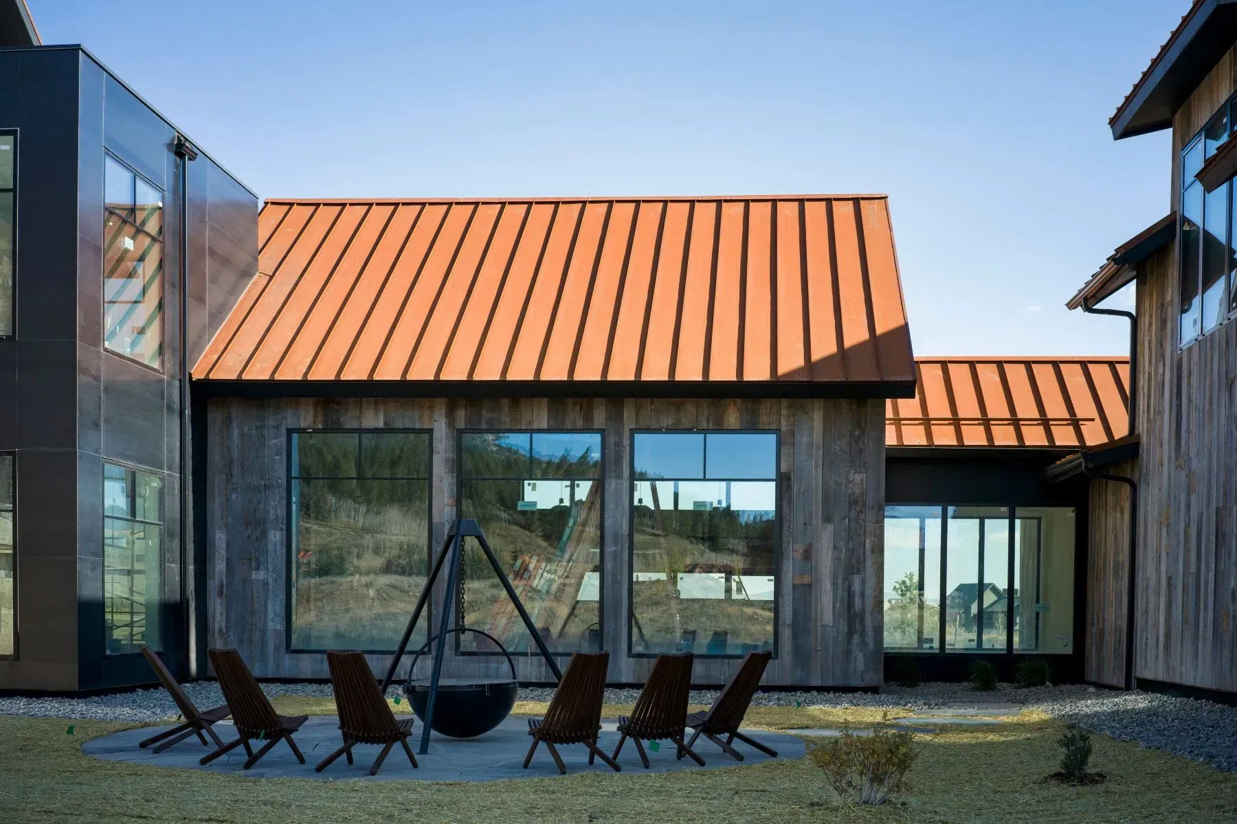 Modern house courtyard with orange metal roofs, glass walls, and chairs around a fire pit