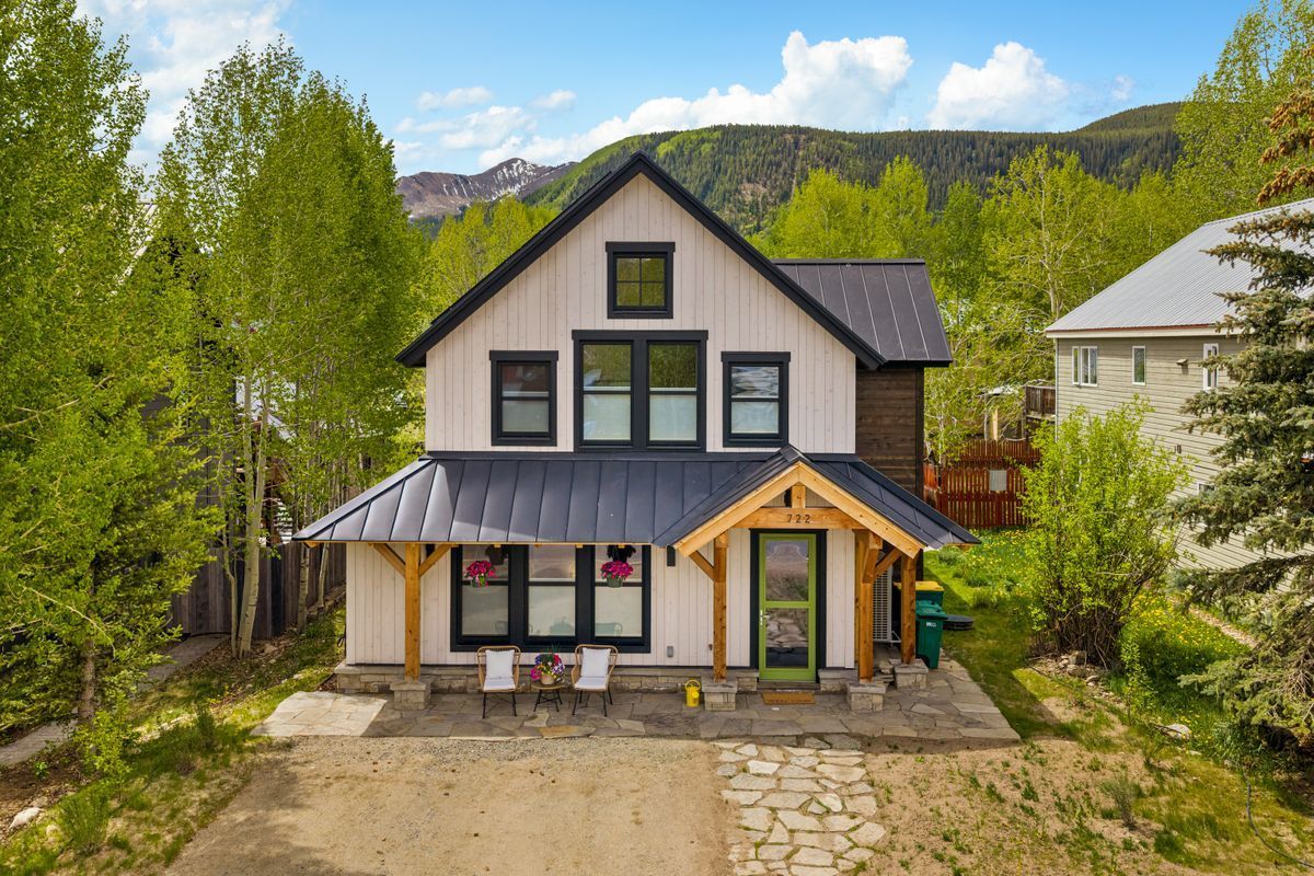 Two-story house with gray roof, white siding, and front porch, surrounded by trees and mountains