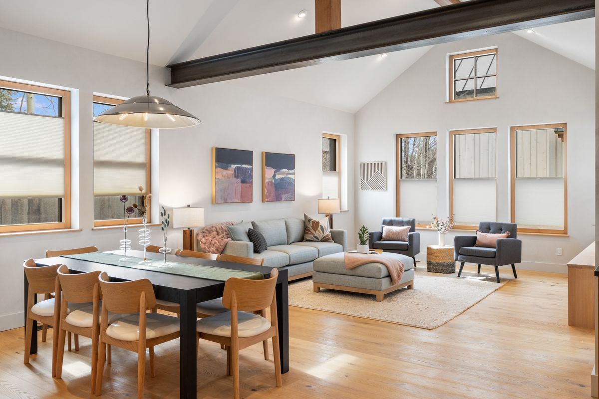 Bright open living room with light wood floors, gray sofa, armchairs, dining table, and large windows