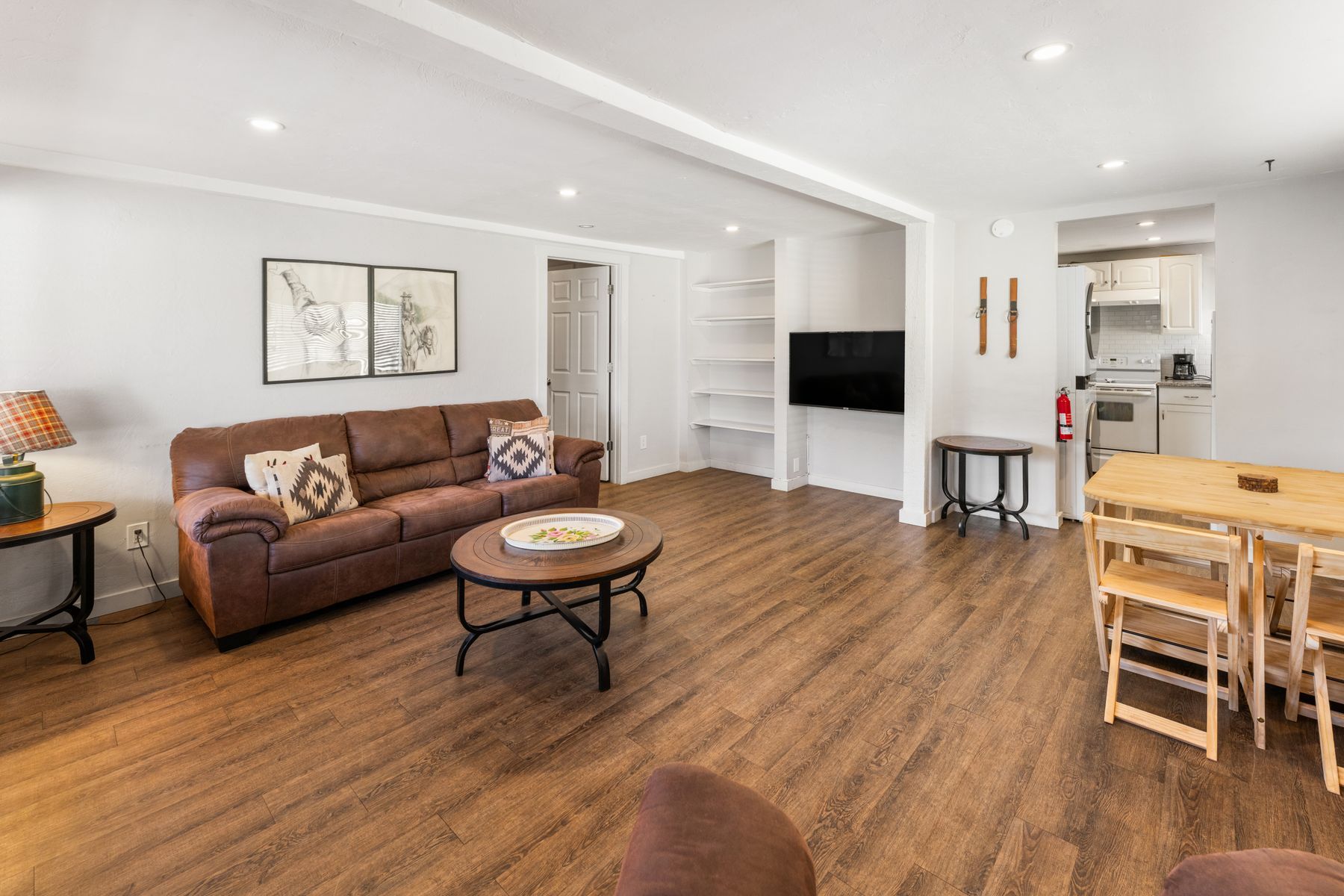 Bright open living room with brown sofa, coffee table, TV, and dining area with wood floors