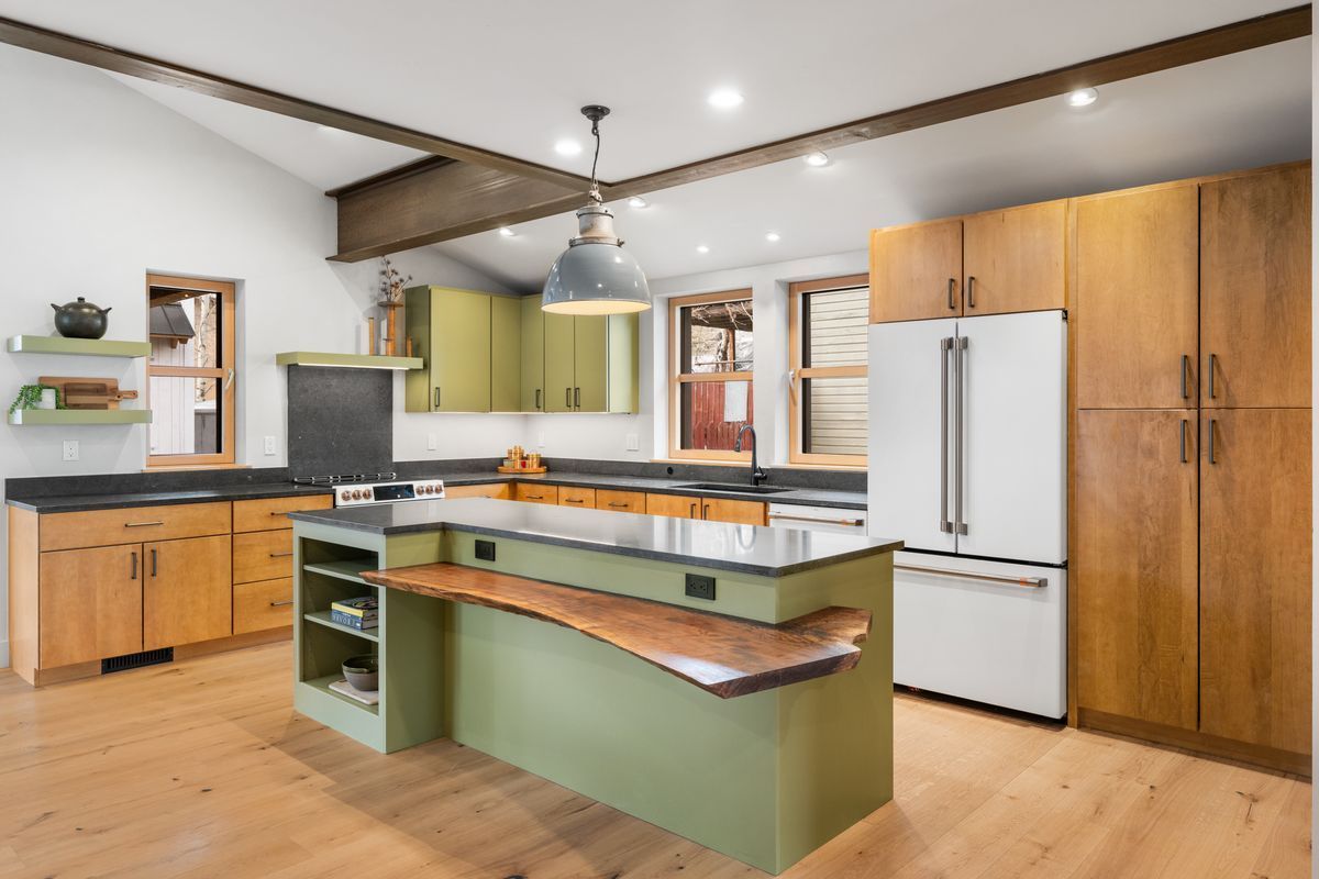 Modern kitchen with green island, wooden cabinets, white appliances, and ceiling fan