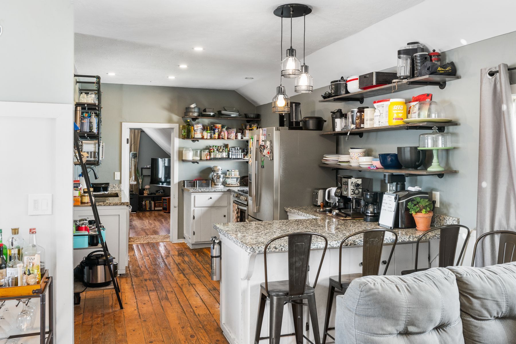 Open kitchen and dining area with bar stools, shelves, and hardwood floors