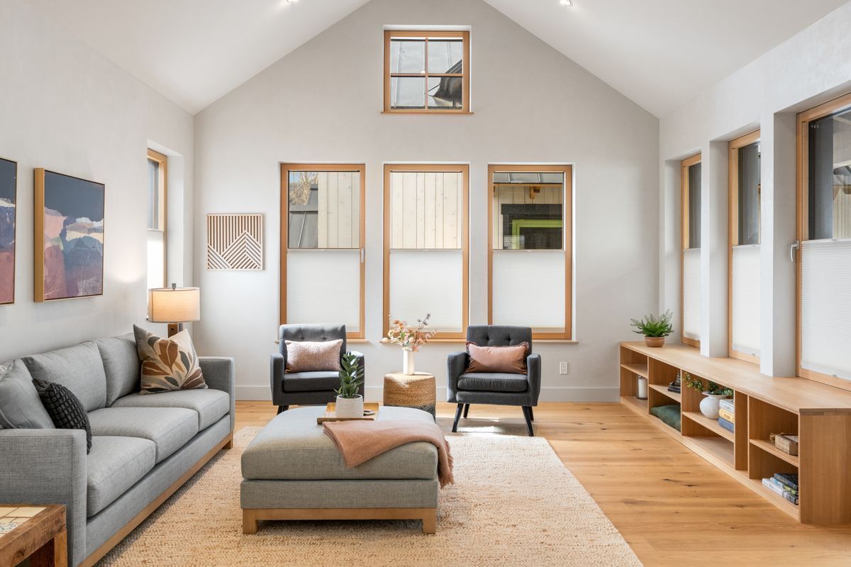Bright living room with gray sofa, two armchairs, wood floors, and large windows in a vaulted space