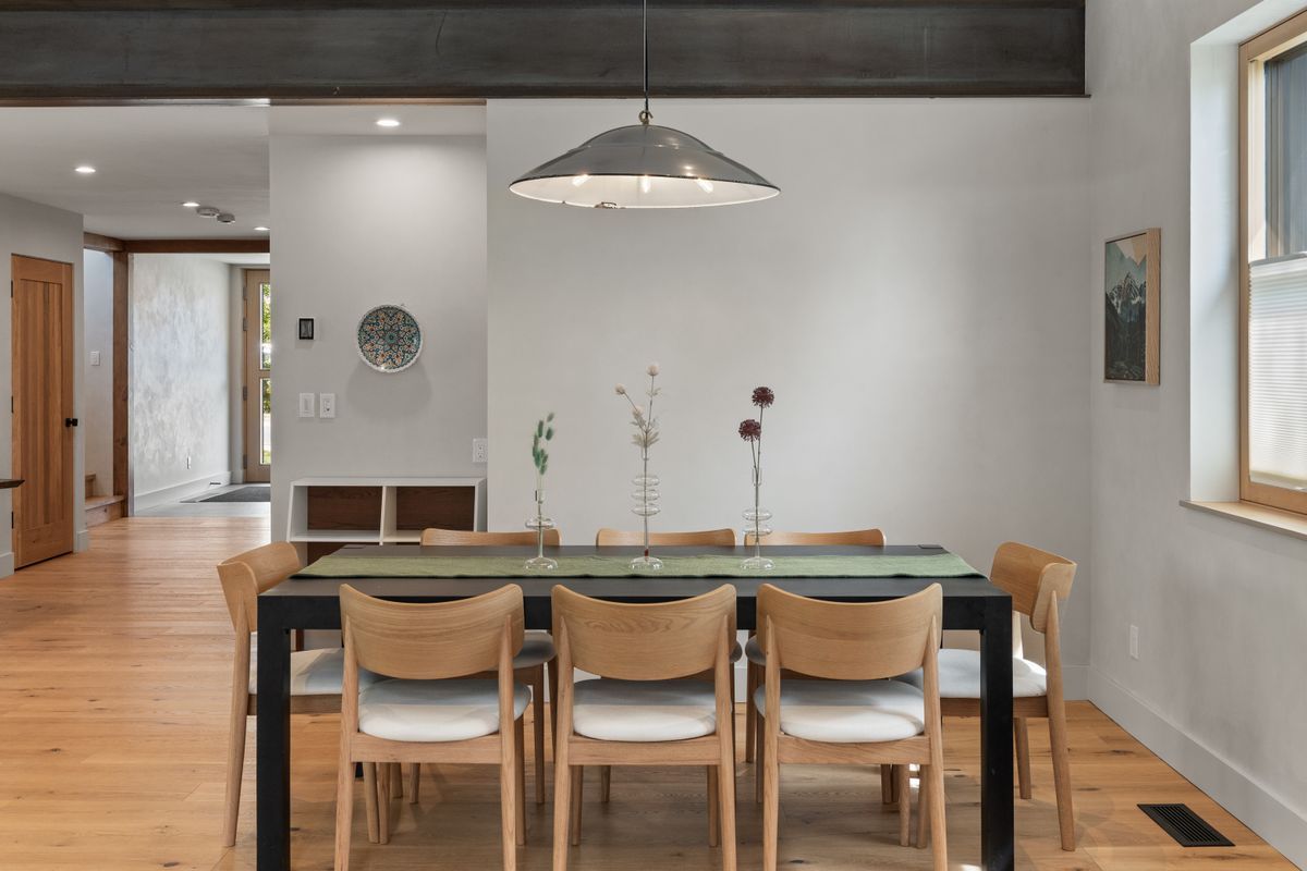 Modern dining room with glass table, wooden chairs, pendant light, and hardwood floors