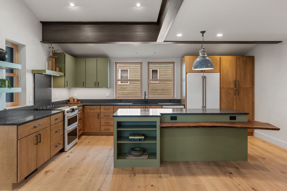 Modern kitchen with wood cabinets, green island, stainless appliances, and light wood floors.