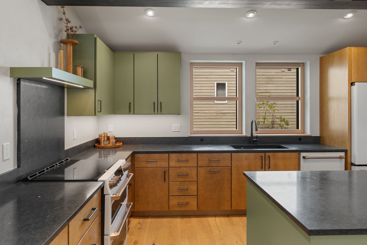 Modern kitchen with green cabinets, black countertops, wooden floor, and a window above the sink