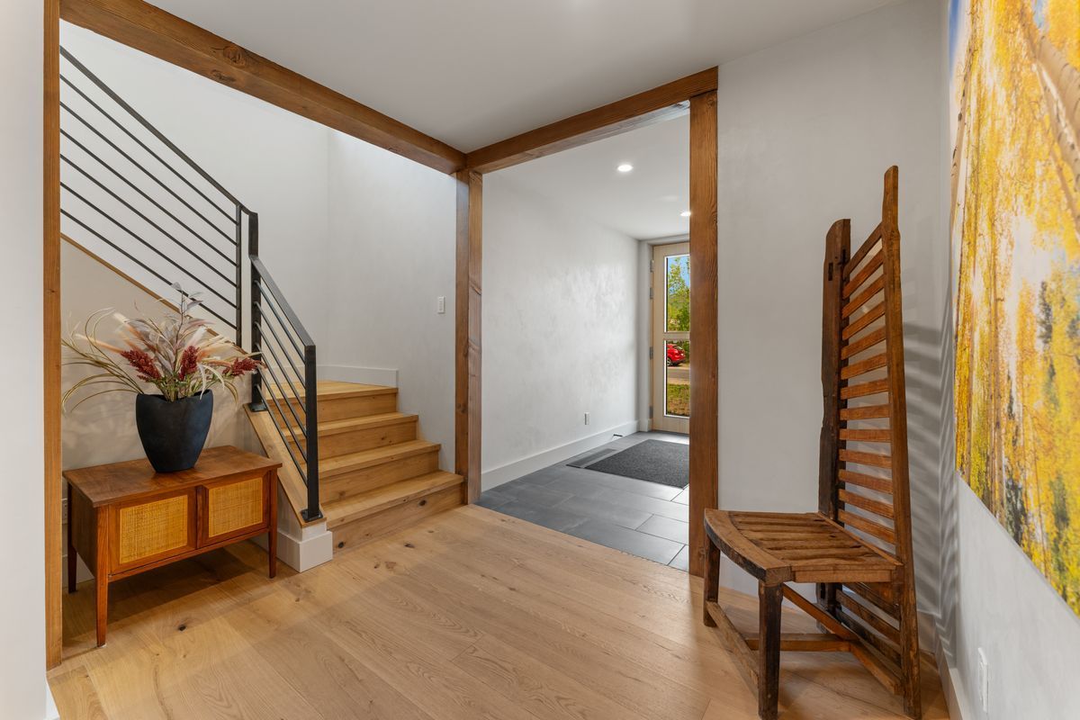 Modern entryway with wooden stairs, light wood floor, bench, and colorful wall art
