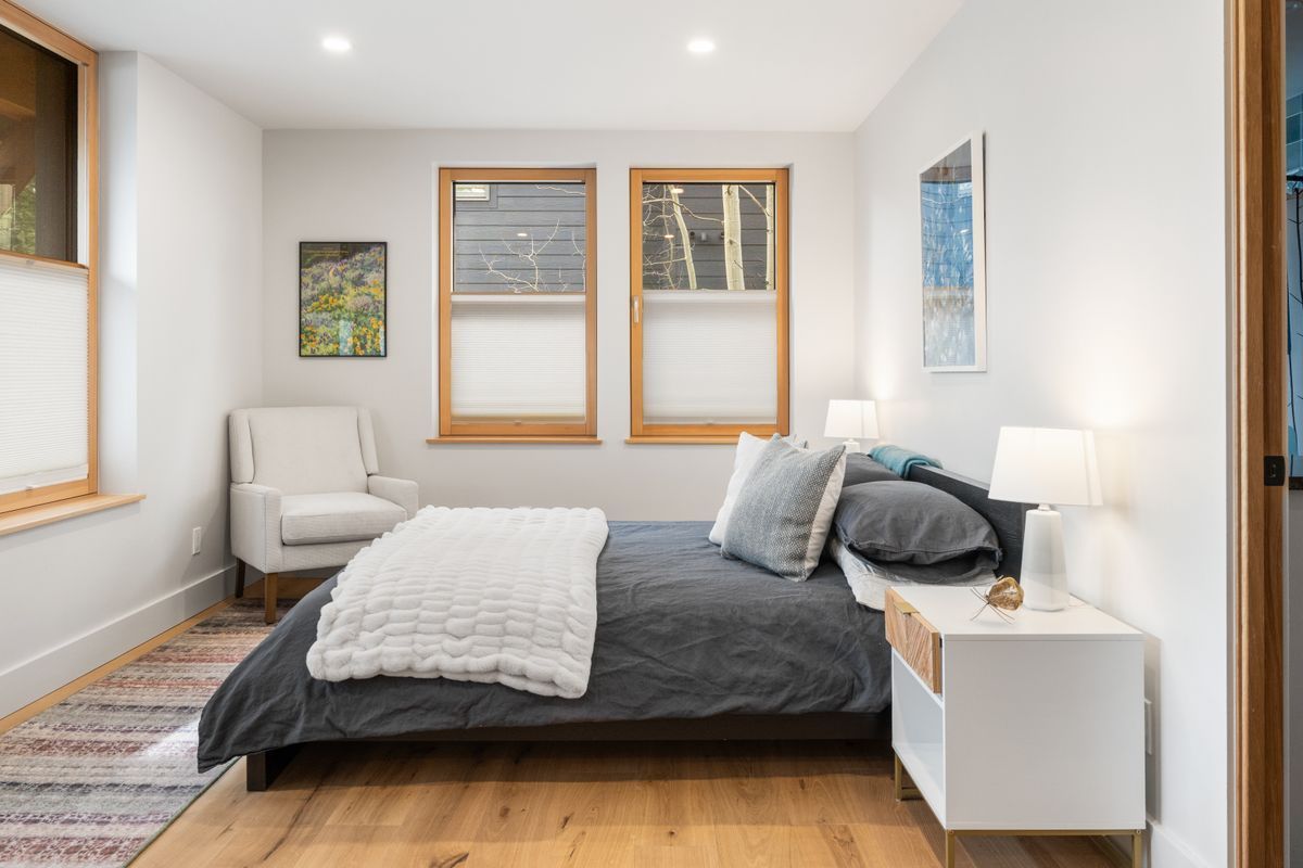 Bright bedroom with a bed, two windows, white chair, and bedside lamps in a minimalist decor