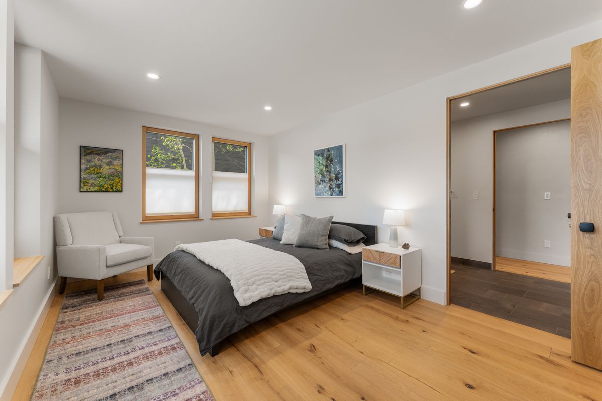 Bright bedroom with bed, chair, two windows, wood floor, and white walls