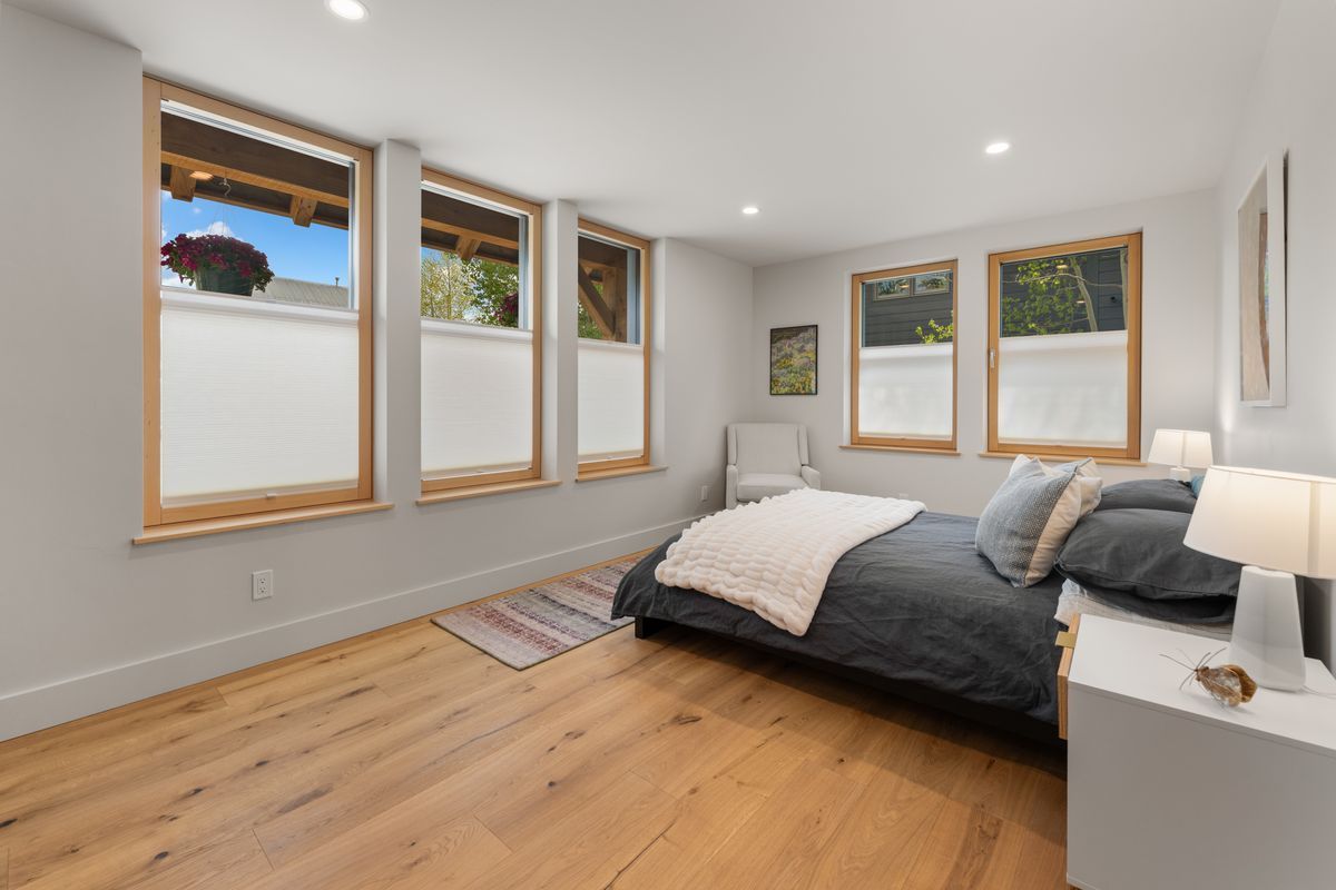 Bright bedroom with wood floors, gray bed, and three windows overlooking a snowy view