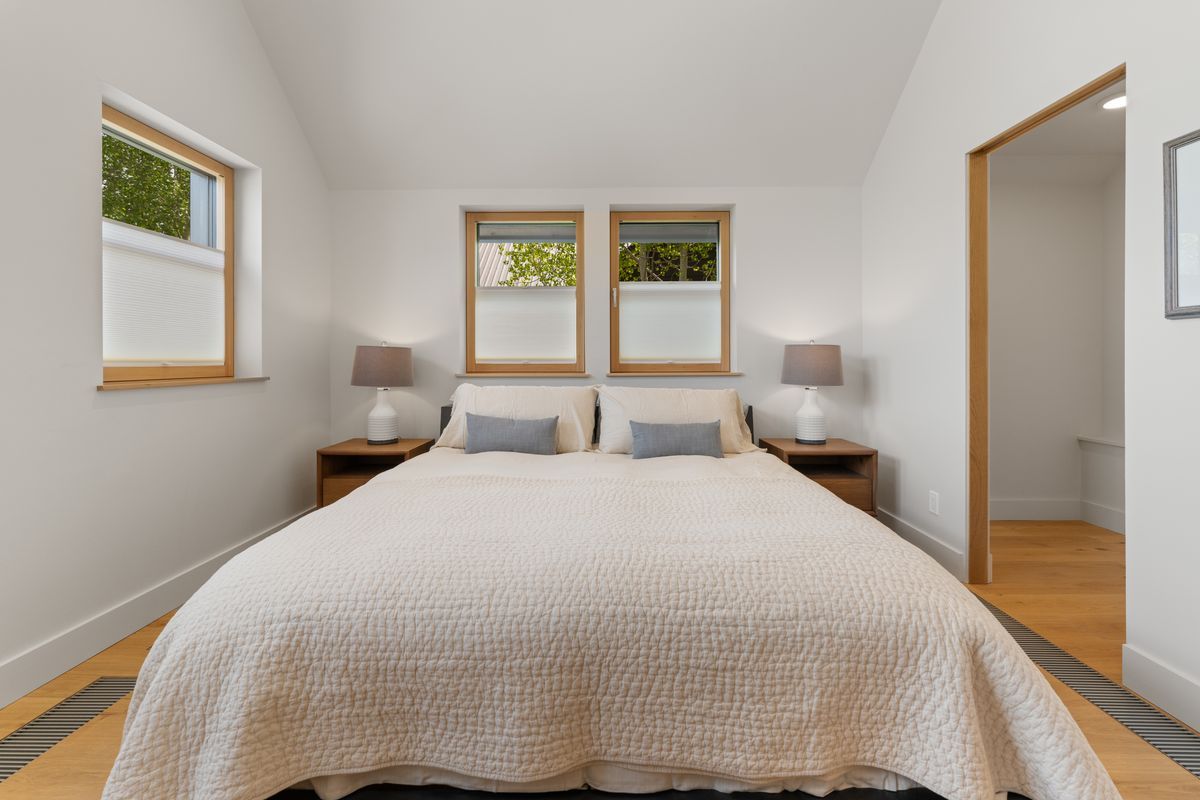 Bright bedroom with a large bed, white walls, and two windows letting in daylight.