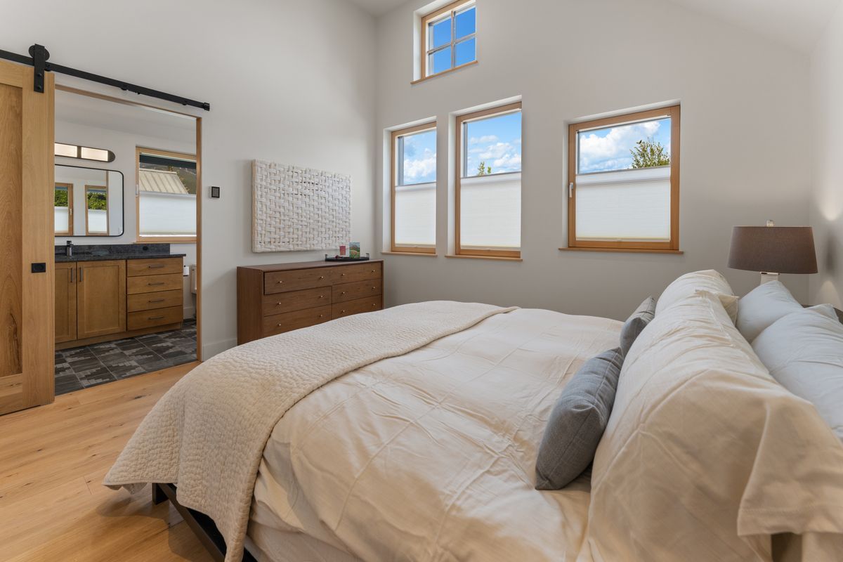 Bright bedroom with a large bed, wood floor, three windows, dresser, and a doorway to a bathroom