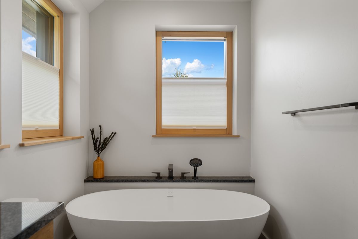Modern bathroom with a freestanding tub, two windows, and white walls