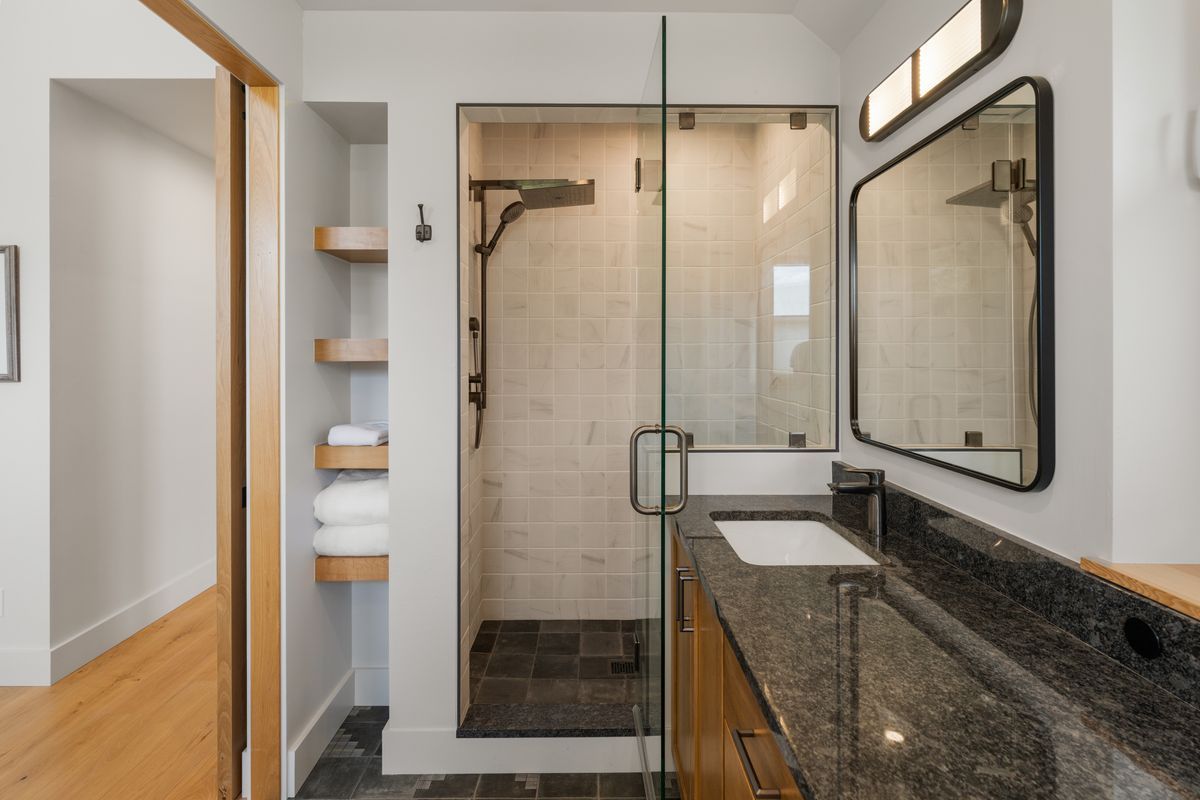 Modern bathroom with glass shower, granite vanity, and open shelving near the doorway