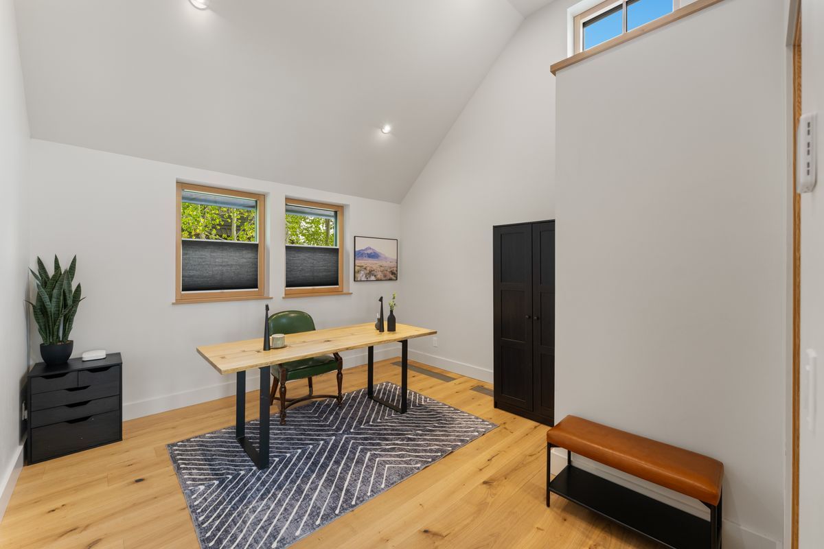 Bright home office with wood table, black chairs, rug, potted plant, and skylight on sloped ceiling