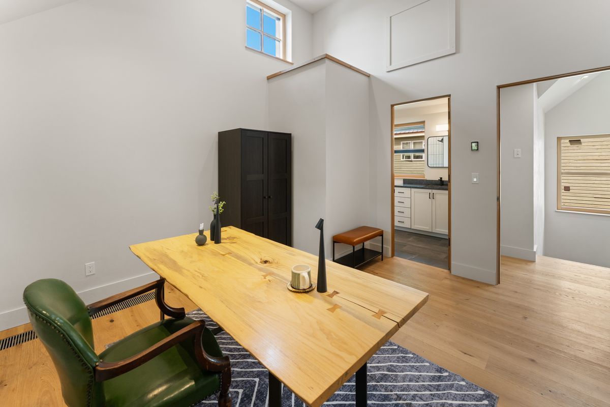 Modern office with wooden desk, green chair, black cabinet, and open doorway in a bright room