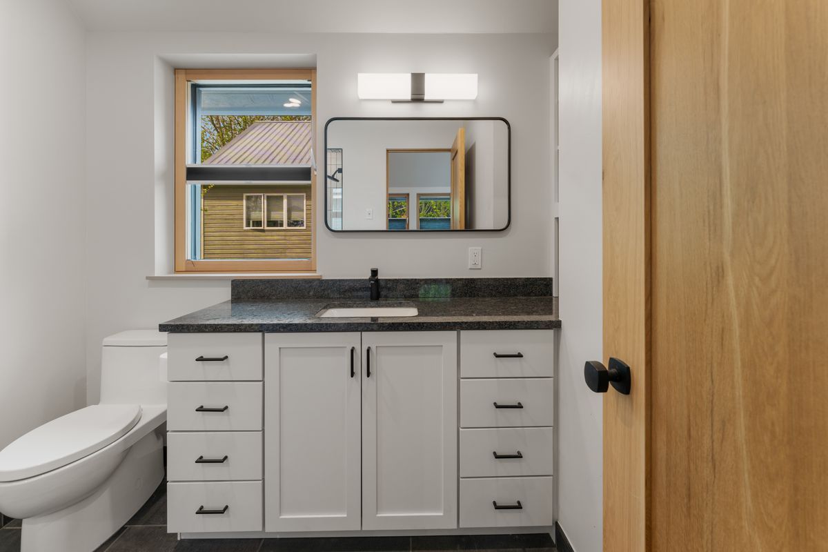Modern bathroom with white vanity, black countertop, mirror, and a window by a wooden door