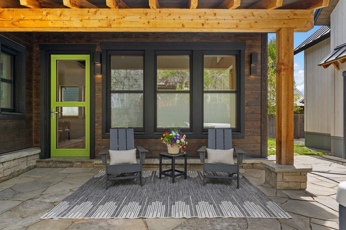 Patio with two chairs and table outside a wooden cabin, with a green-trimmed door and windows