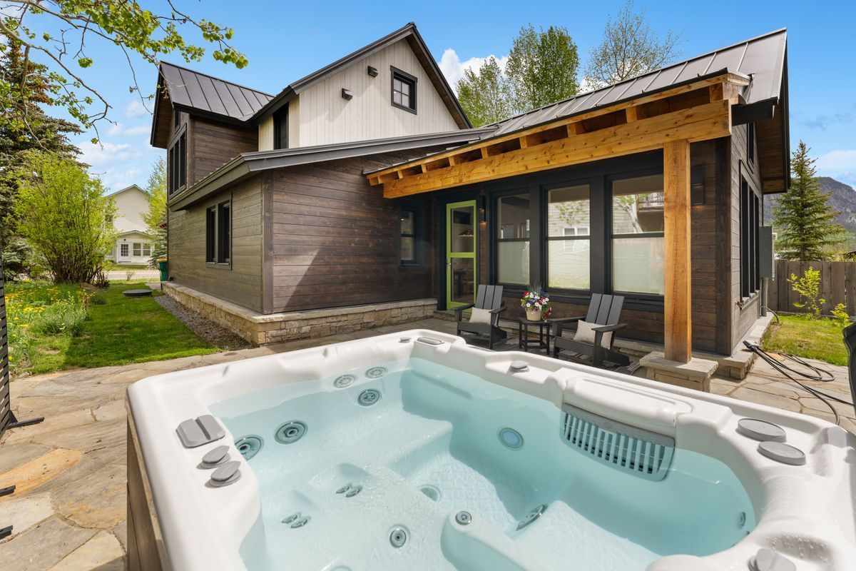 Backyard hot tub beside a modern rustic house under a covered patio