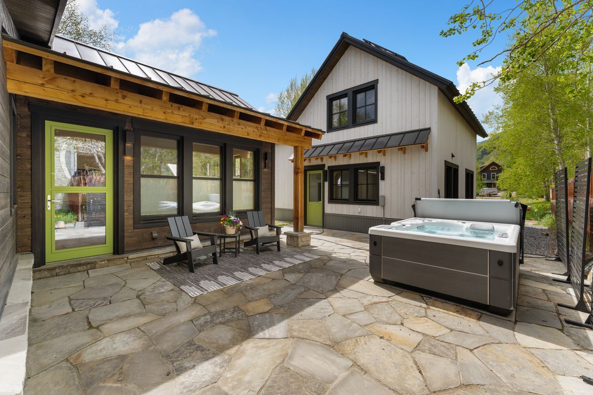 Patio with stone paving, outdoor seating, and hot tub beside a modern house and screened porch