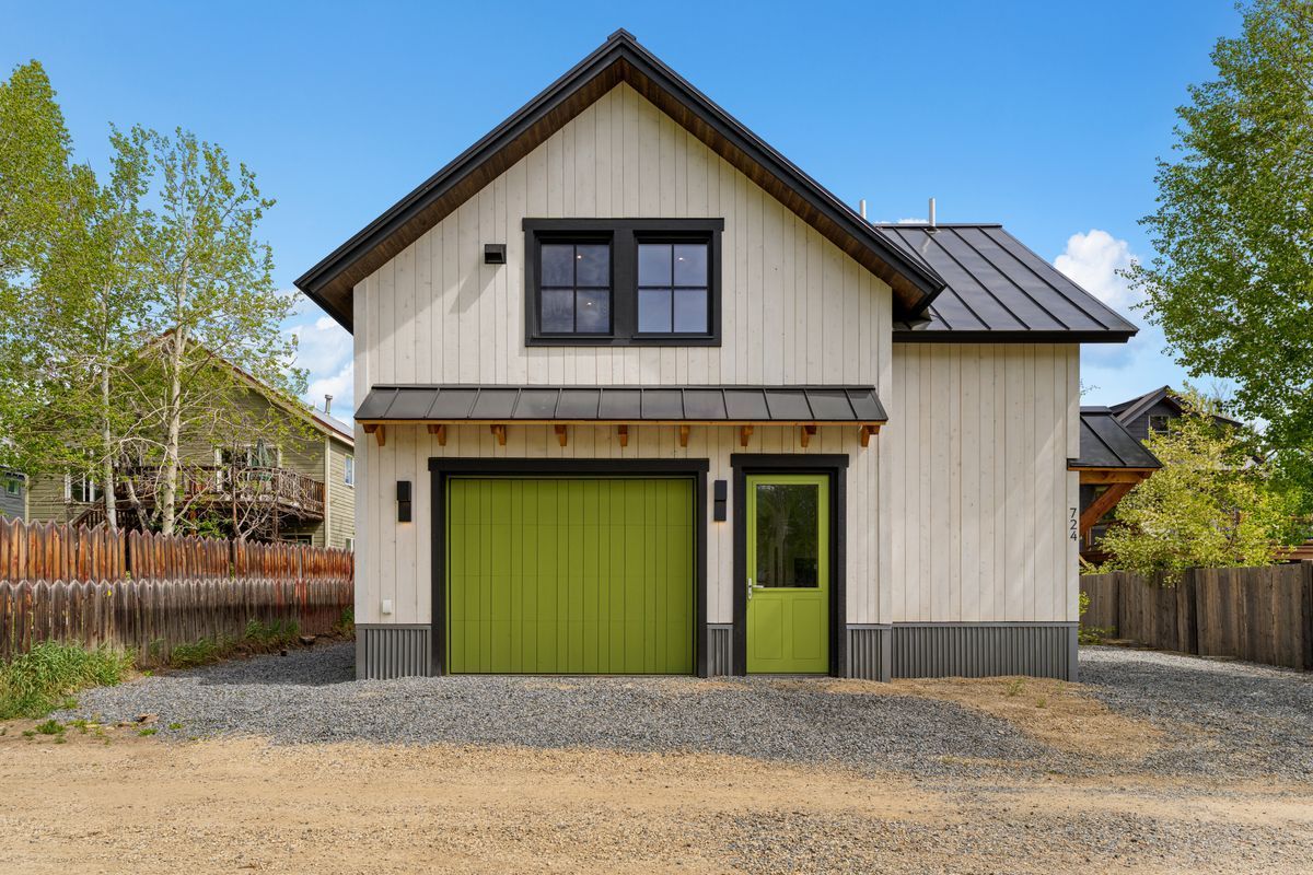 Modern two-story house with olive green garage door and trim, beige siding, and gravel driveway under a blue sky