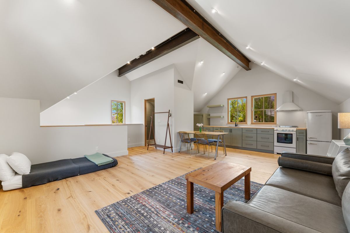Loft living room with sofa, rug, coffee table, and kitchen area under vaulted ceiling