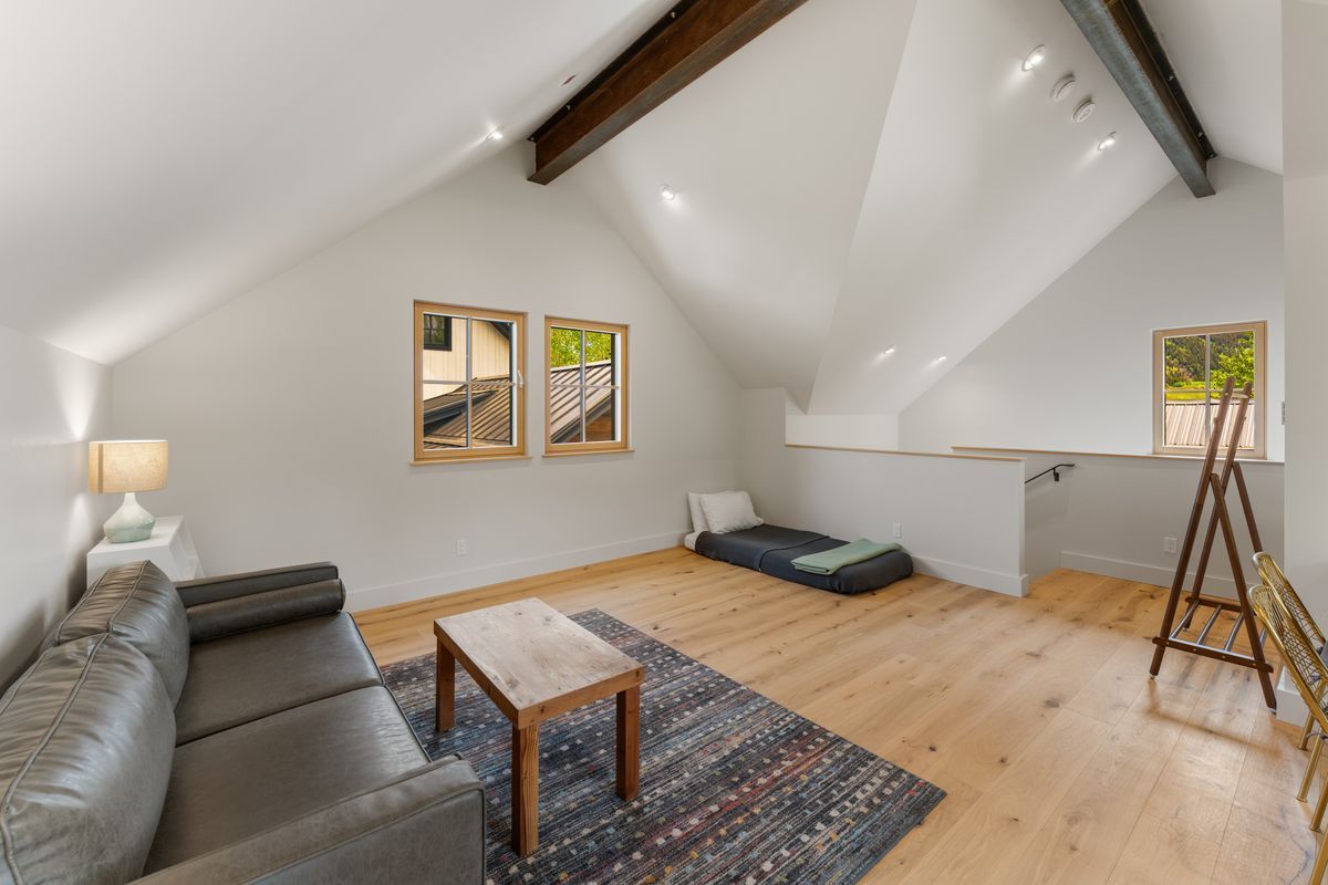Bright attic living room with gray sofa, patterned rug, low table, and exposed beams.