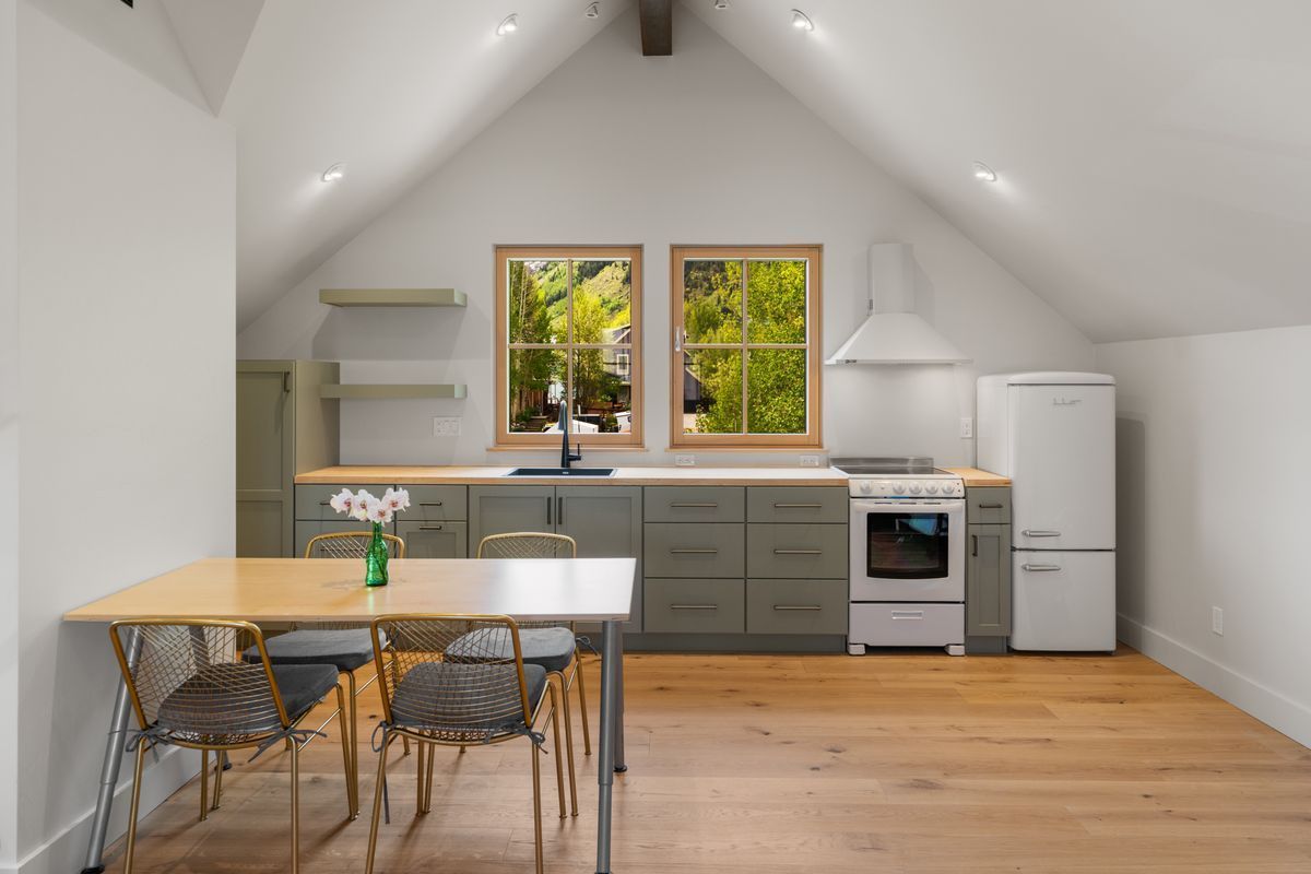 Bright loft kitchen with white walls, wood floors, dining table, and two windows over the sink