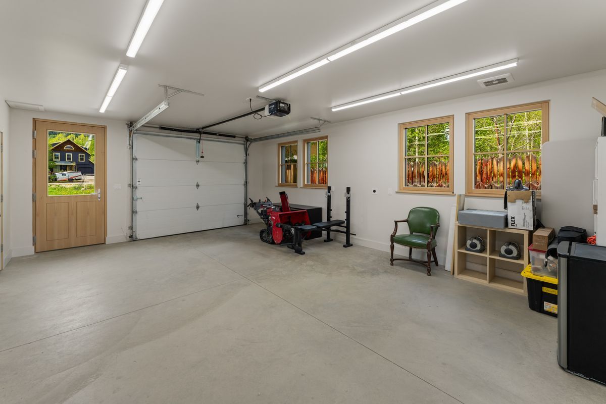 Empty garage with white walls, concrete floor, garage door, windows, and tools/storage along the right wall